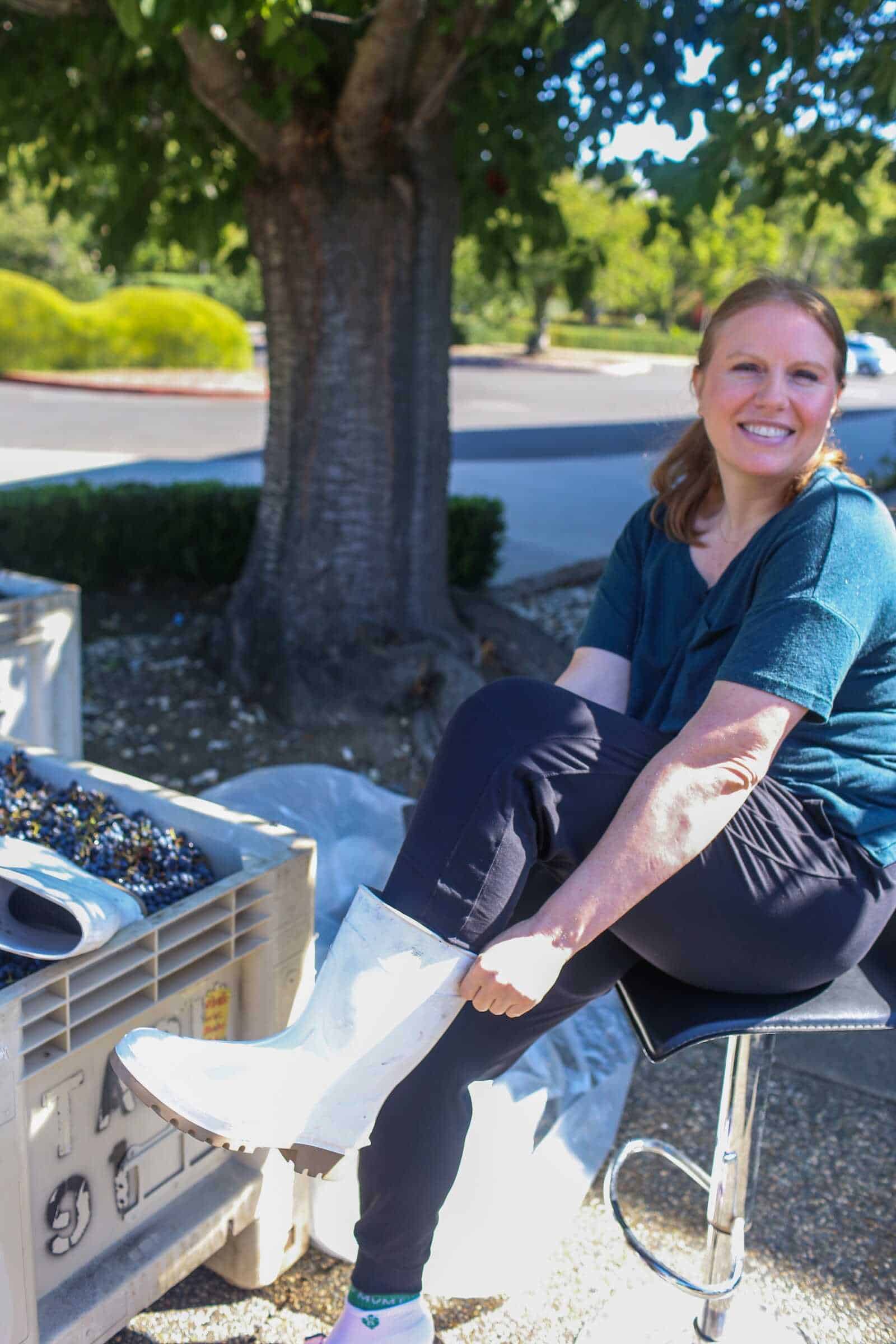 Comfortable woman in rubber boots sitting outdoors on sunny day.