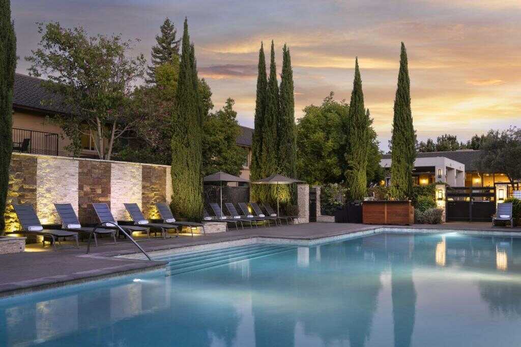 Serene outdoor swimming pool with lounge chairs and lush greenery at twilight.