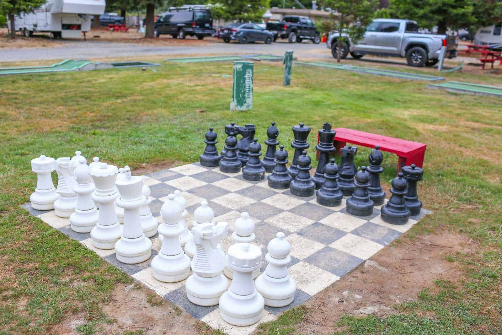 Large outdoor chessboard with black and white pieces, situated in a grassy park area in California.
