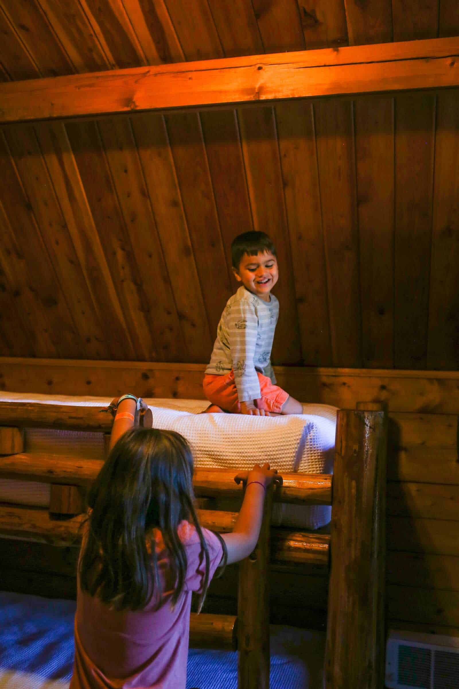 Cozy cabin bedroom with children playing on bunk beds, rustic wood interior.