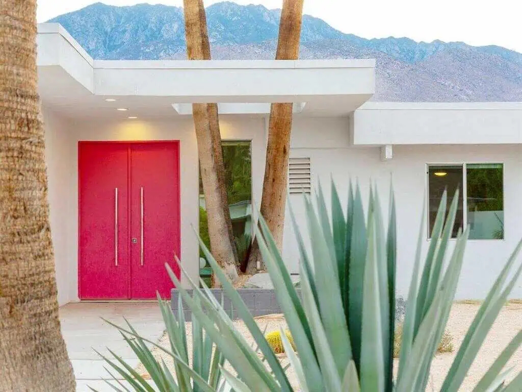 Modern house with vibrant pink door and desert landscaping in California nomad style.