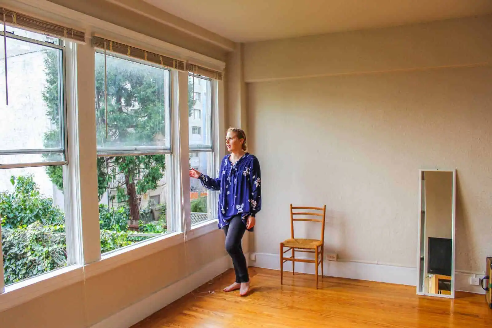 Bright woman looking out of large windows in a minimalist apartment, natural light, urban view, California Nomad lifestyle.