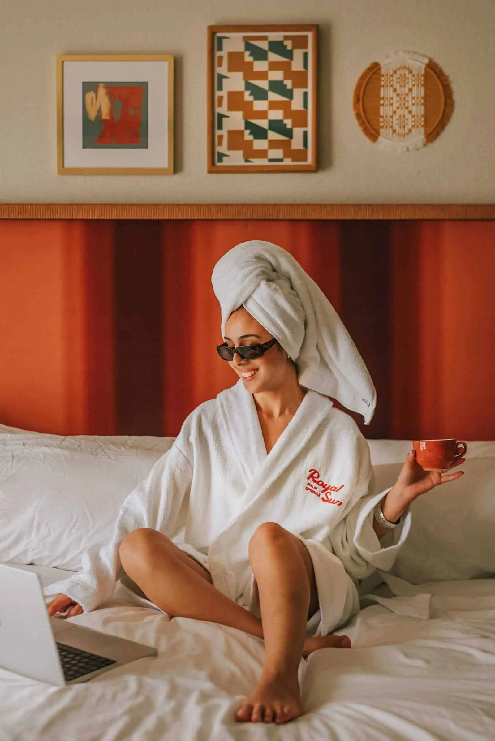 Relaxed woman in a spa hotel room wearing a white bathrobe and towel, enjoying a cup of coffee.