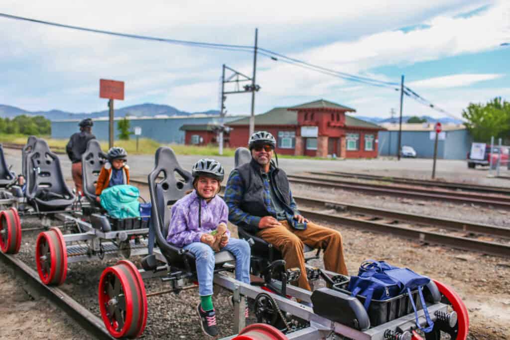 Father and daughter seated on Skunk Train Railcoaster Railbikes wearing helmets at the rail yard.
