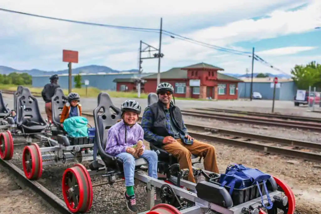 Father and daughter seated on Skunk Train Railcoaster Railbikes wearing helmets at the rail yard.